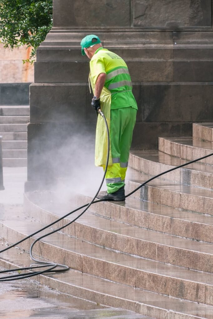 A street worker pressure washes stone stairs in a public park, ensuring cleanliness and safety.